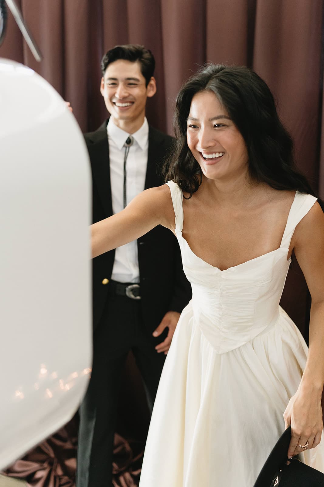 A newlywed couple stepping up to the MEMORI booth, the bride laughing as she reaches for the screen.