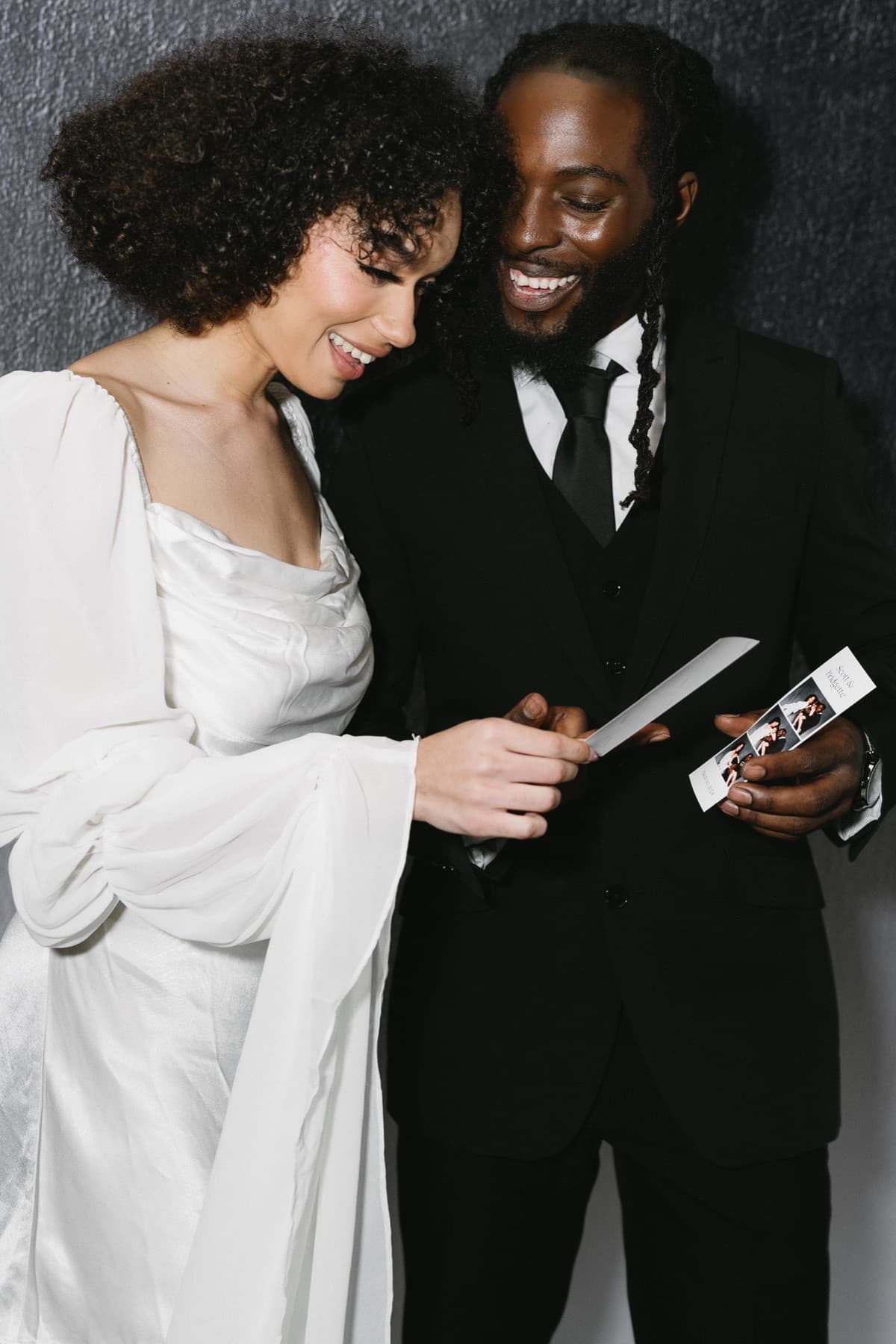 A bride and groom laughing together as they look over their photo strip from the MEMORI booth at their wedding reception.