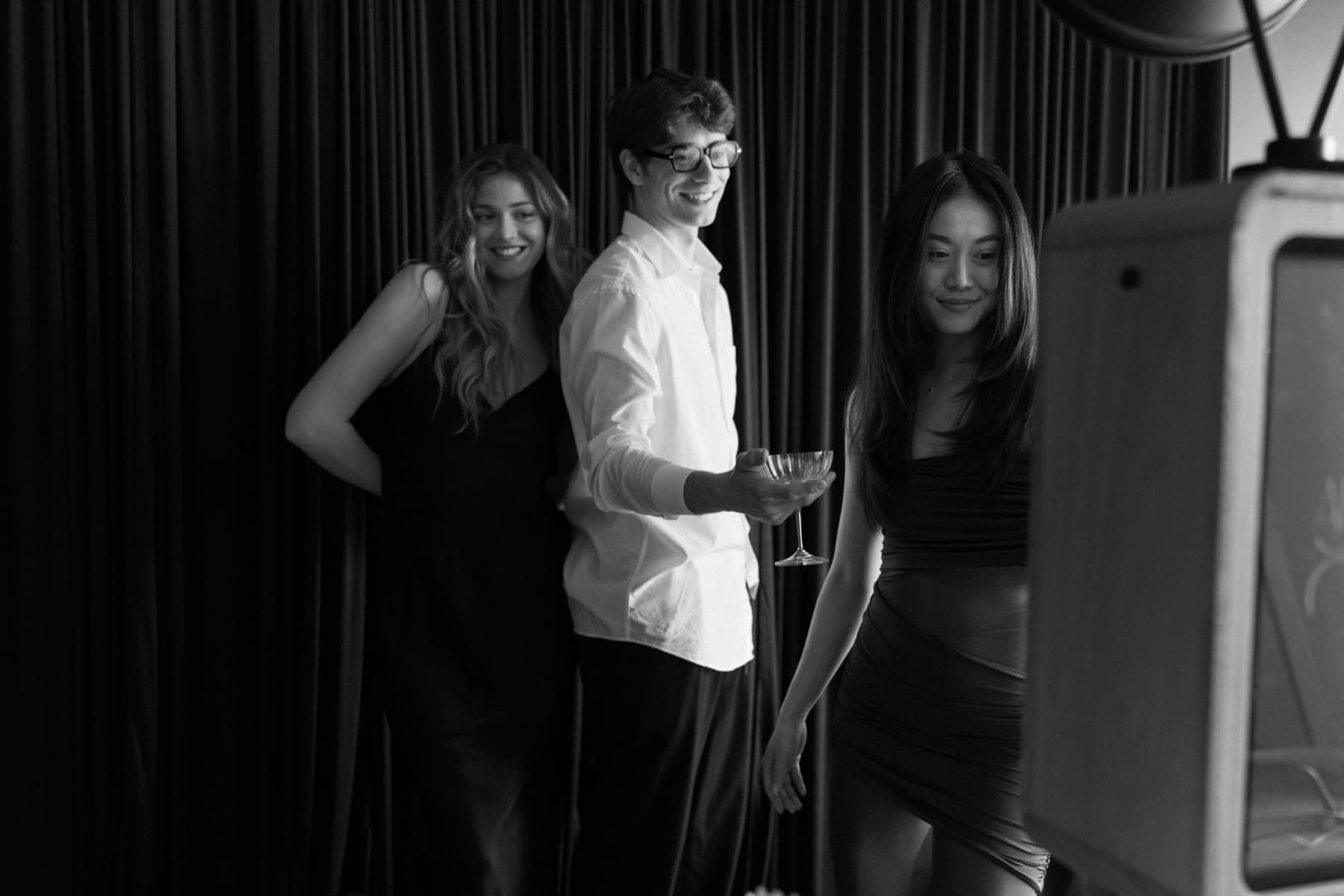 Three guests laughing together at the MEMORI photo booth in front of a dark velvet curtain.