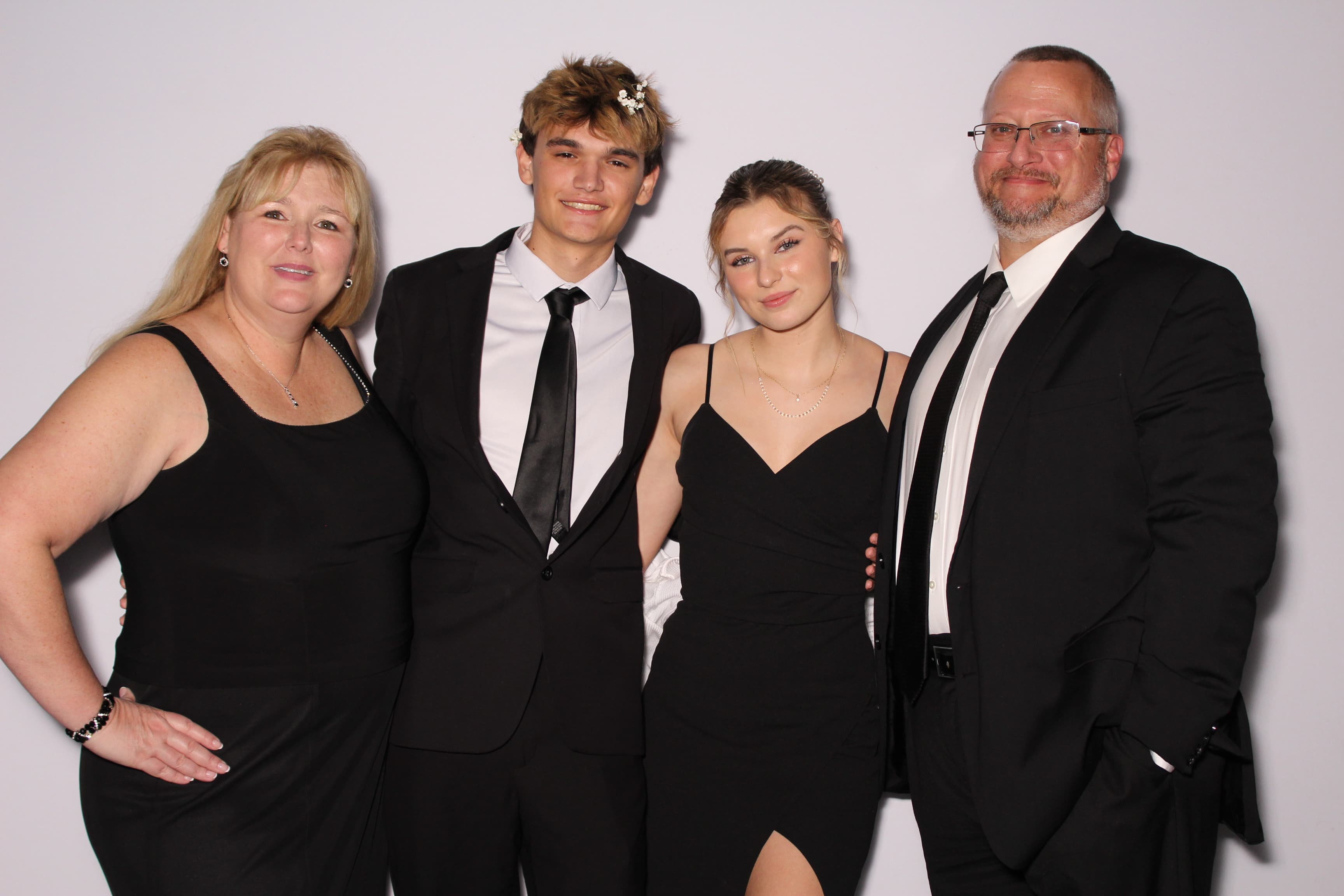 A family of four dressed in formal black attire smiling together in front of a plain white backdrop.