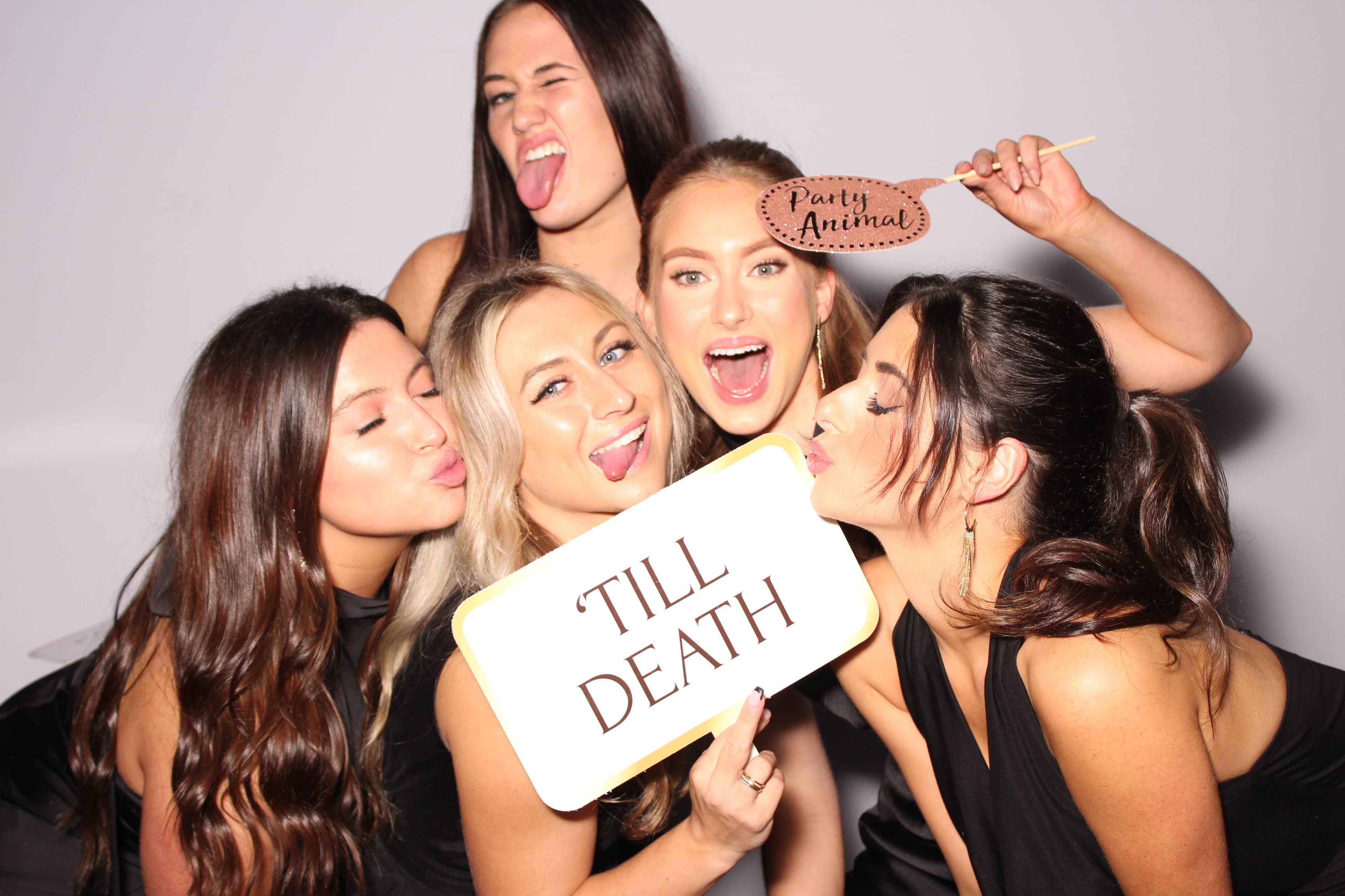 A group of friends in black dresses making playful faces with ‘Party Animal’ and ‘’Till Death’ signs.