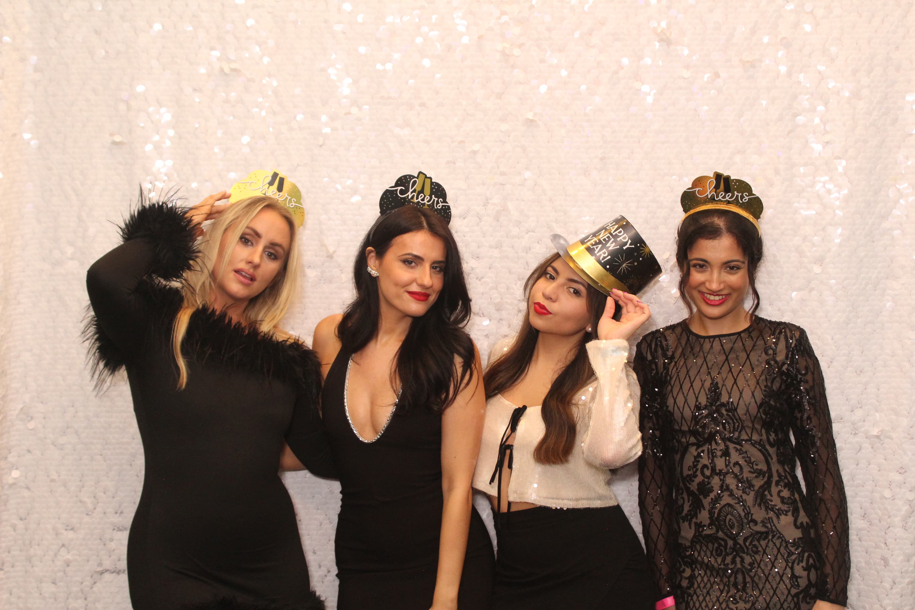 Four friends wearing sparkly New Year’s crowns and a top hat, celebrating together against a sequin backdrop.