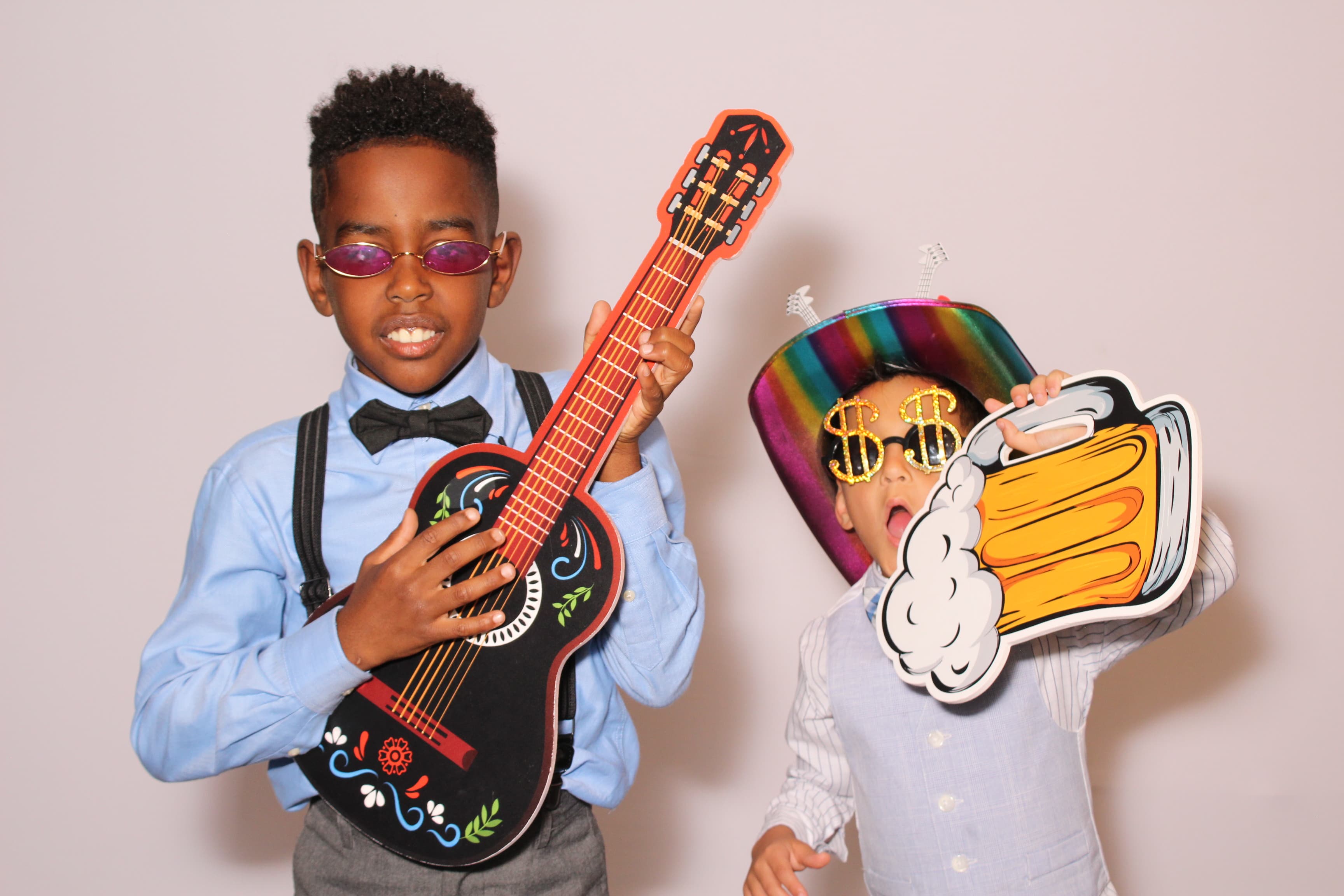 Two kids goofing around with a toy guitar and a giant foam beer-mug prop.