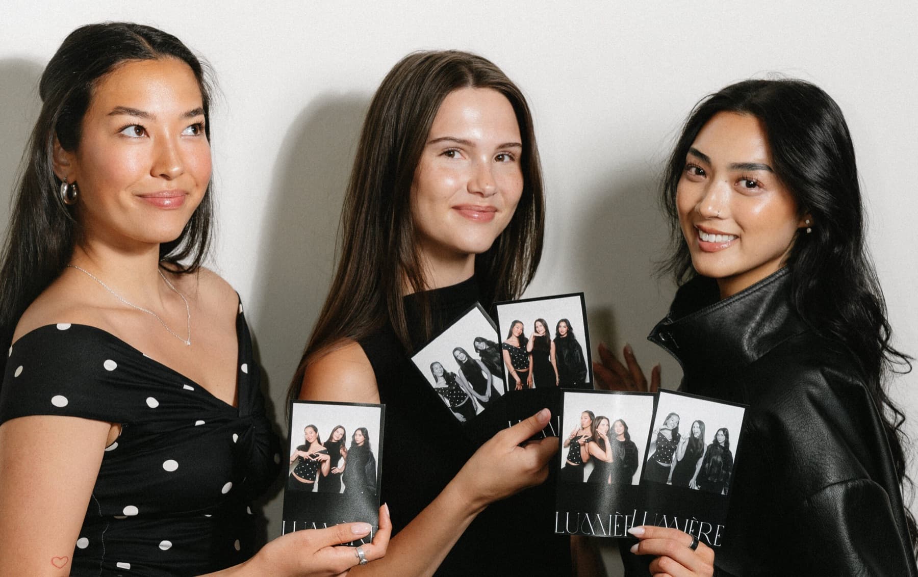 Three friends posing with their black-and-white photo strips at the MEMORI booth.