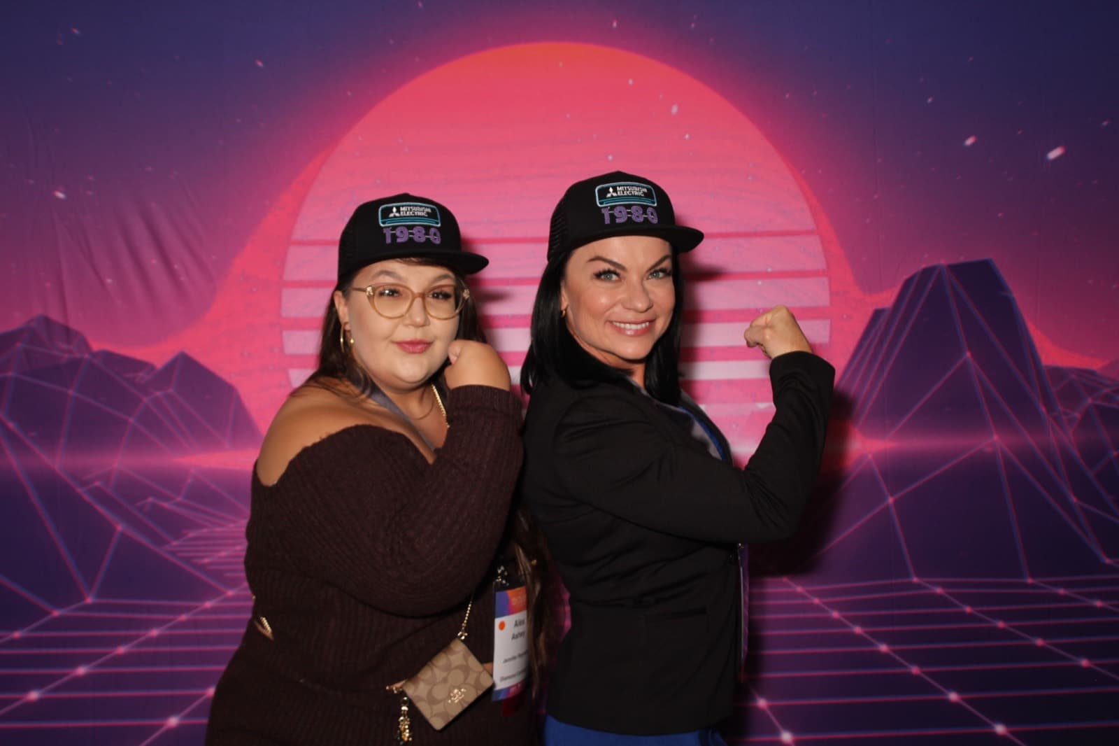 Two colleagues in matching event hats flexing for the camera.