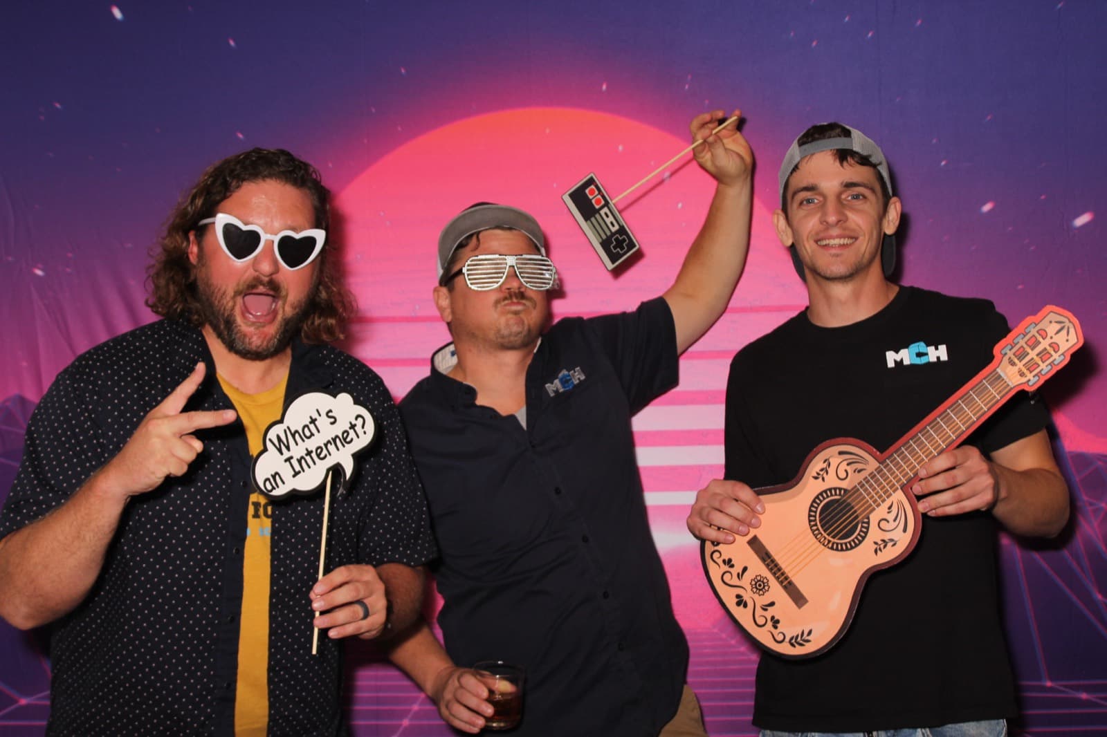 Three coworkers hamming it up with heart sunglasses, a toy guitar and sign props.