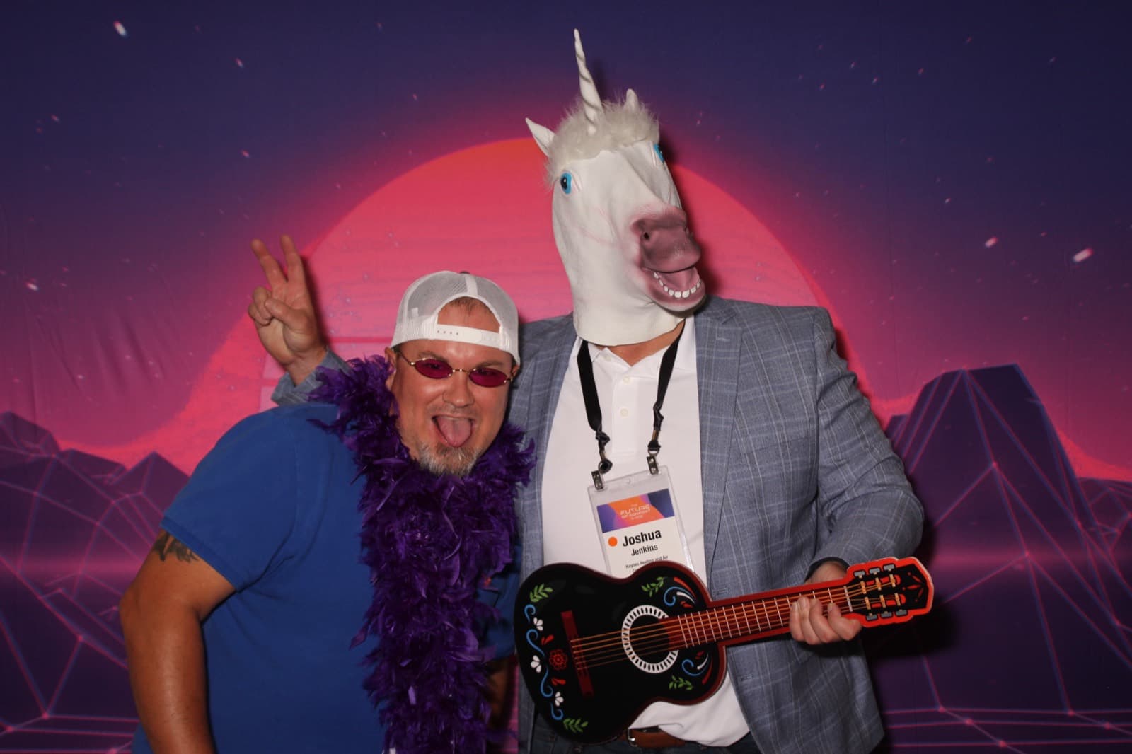 A guest in a feather boa posing beside a coworker wearing a unicorn mask.