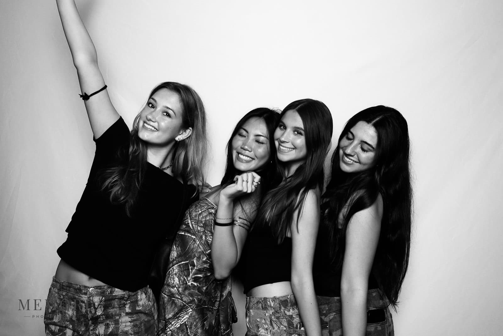 Four friends posing together, one with her arm raised, in a black and white glam booth portrait.