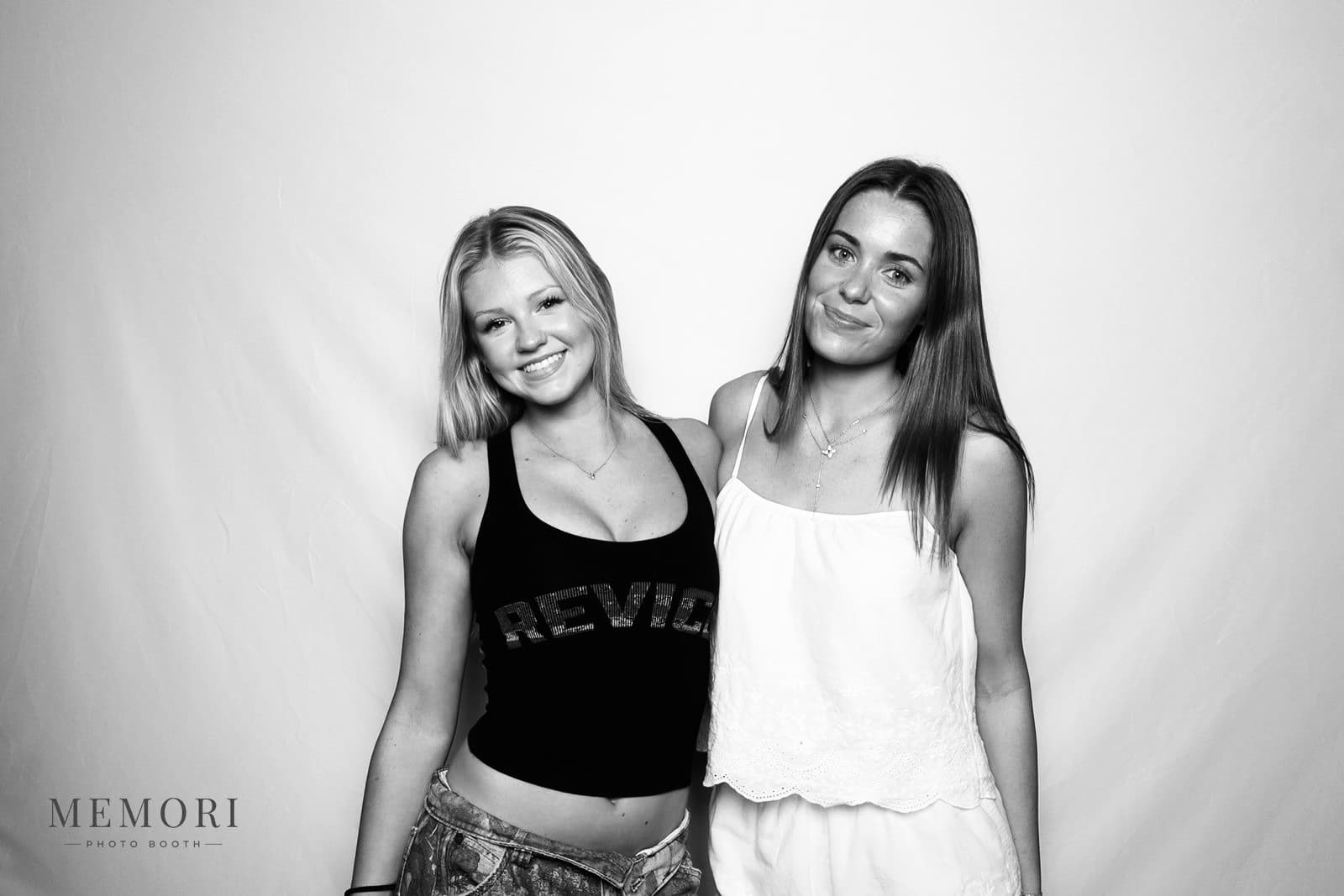 Two friends smiling side by side in a black and white glam booth portrait against a white backdrop.
