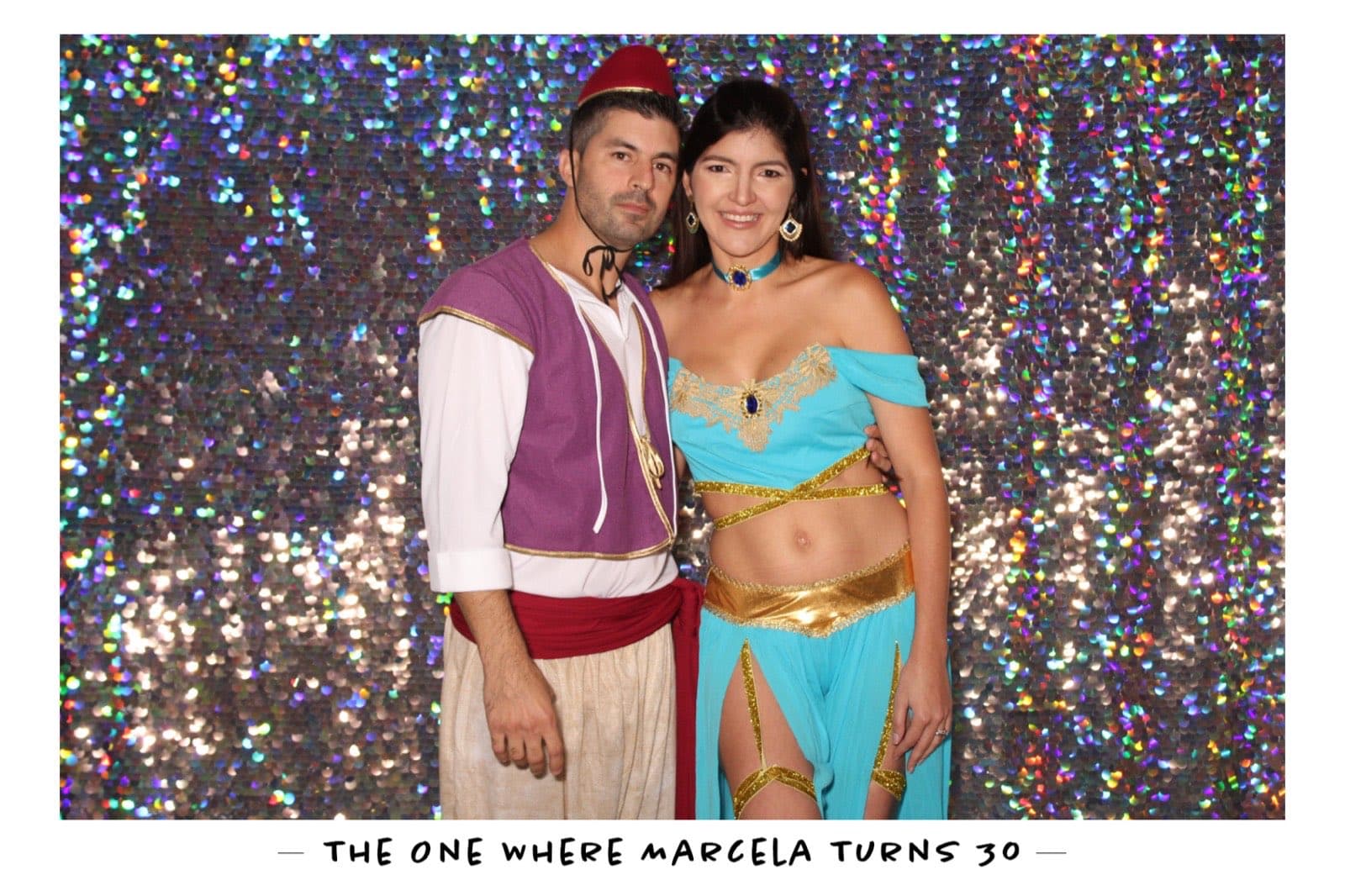 A couple dressed as Aladdin and Jasmine on a rainbow sequin backdrop at Marcela's 30th birthday.
