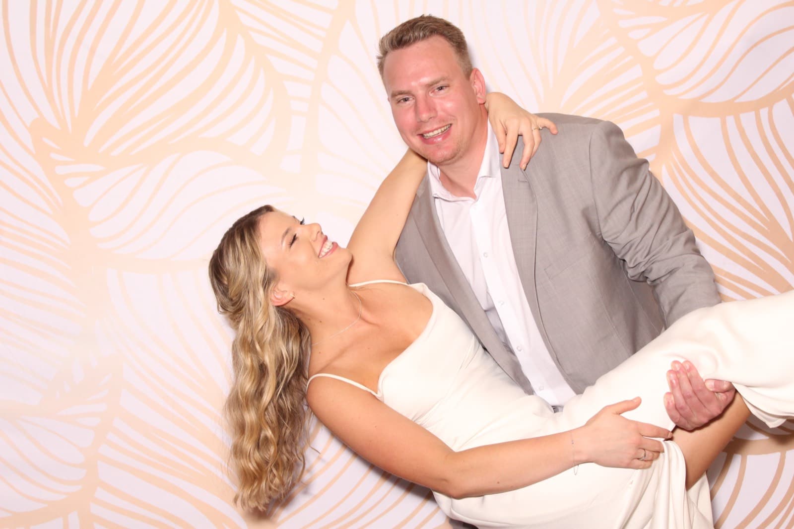 A groom dipping his laughing bride in front of a blush floral backdrop at the MEMORI booth.