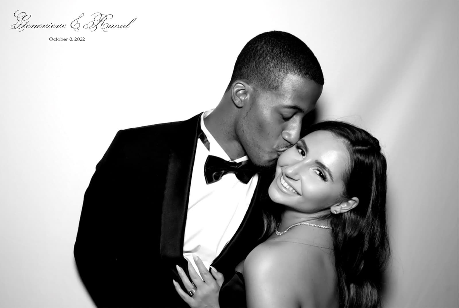 Black and white glam portrait of a groom in a velvet tuxedo kissing his smiling bride's cheek.