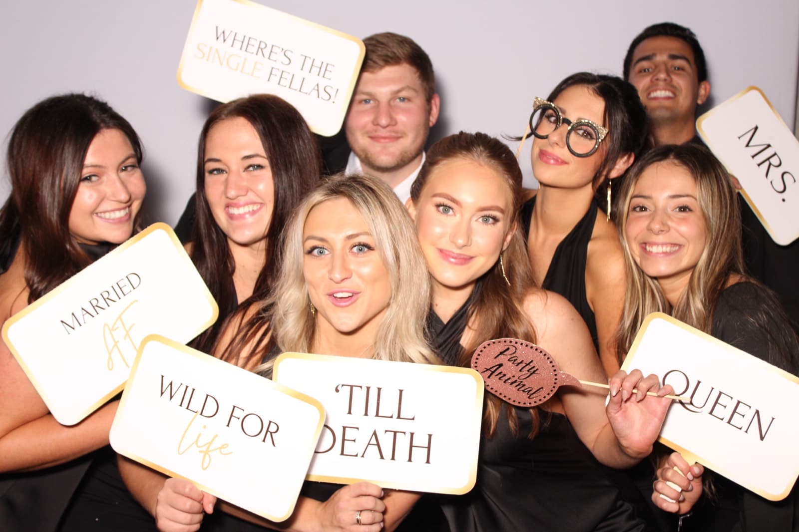 Bridesmaids crowding in with 'Till Death' and 'Wifey' sign props.